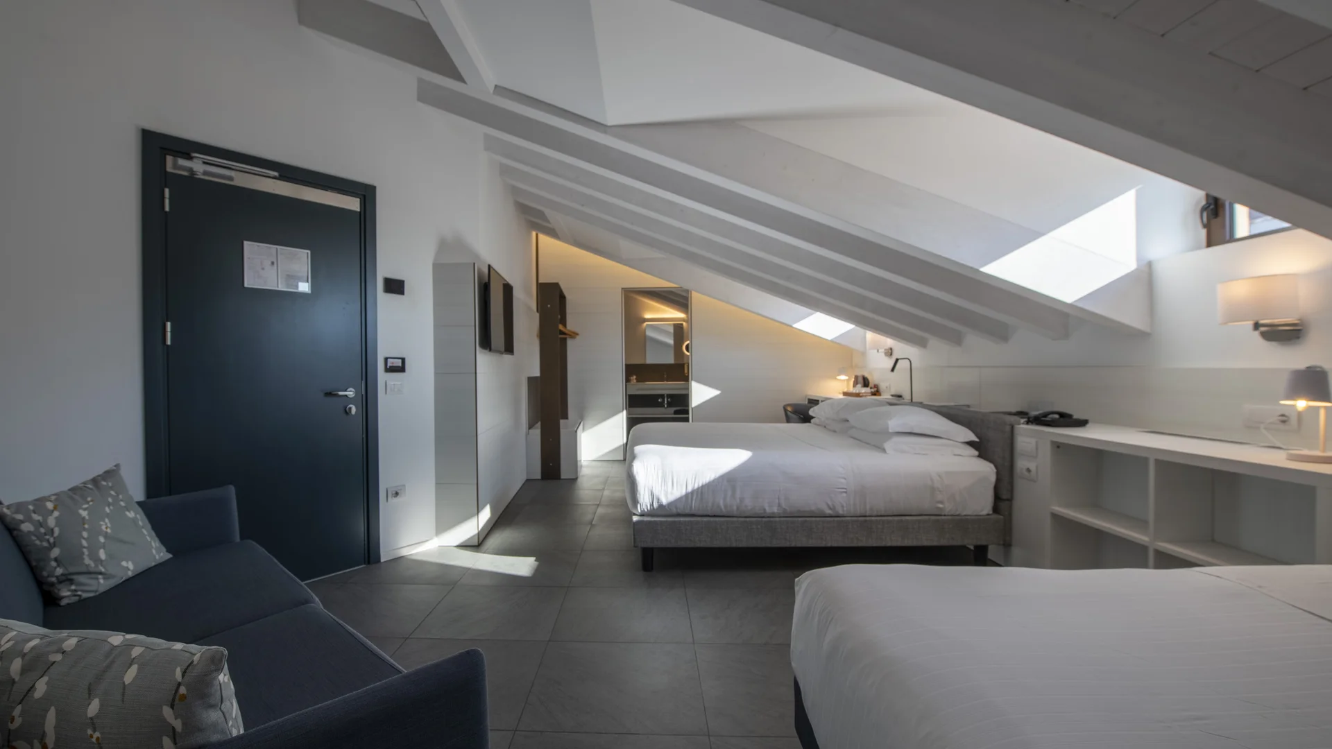 Modern attic hotel room with two beds, a sofa, desk and skylight