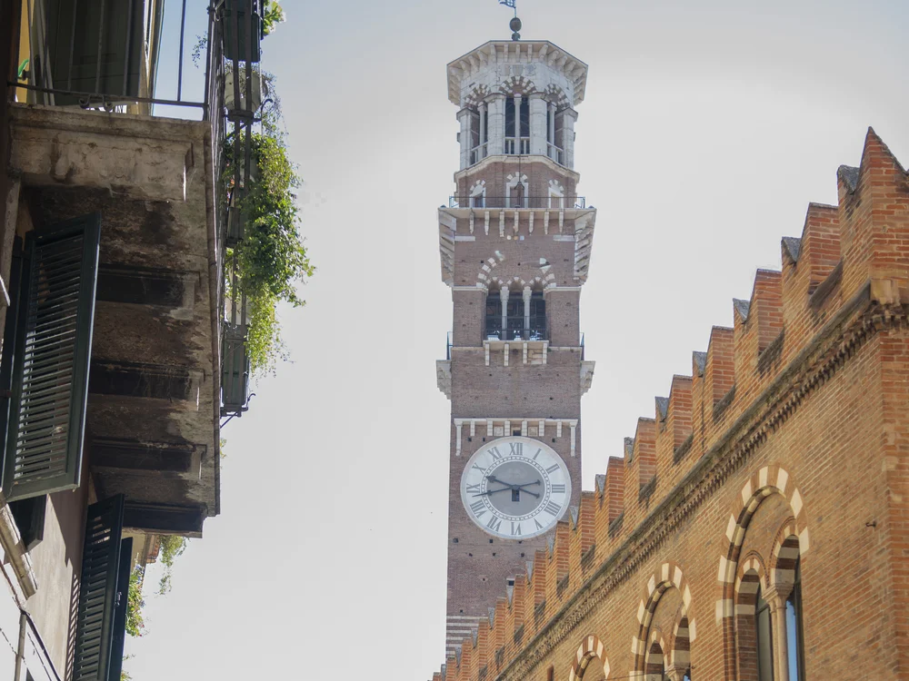 Clock tower above a narrow street lined with brick arcades