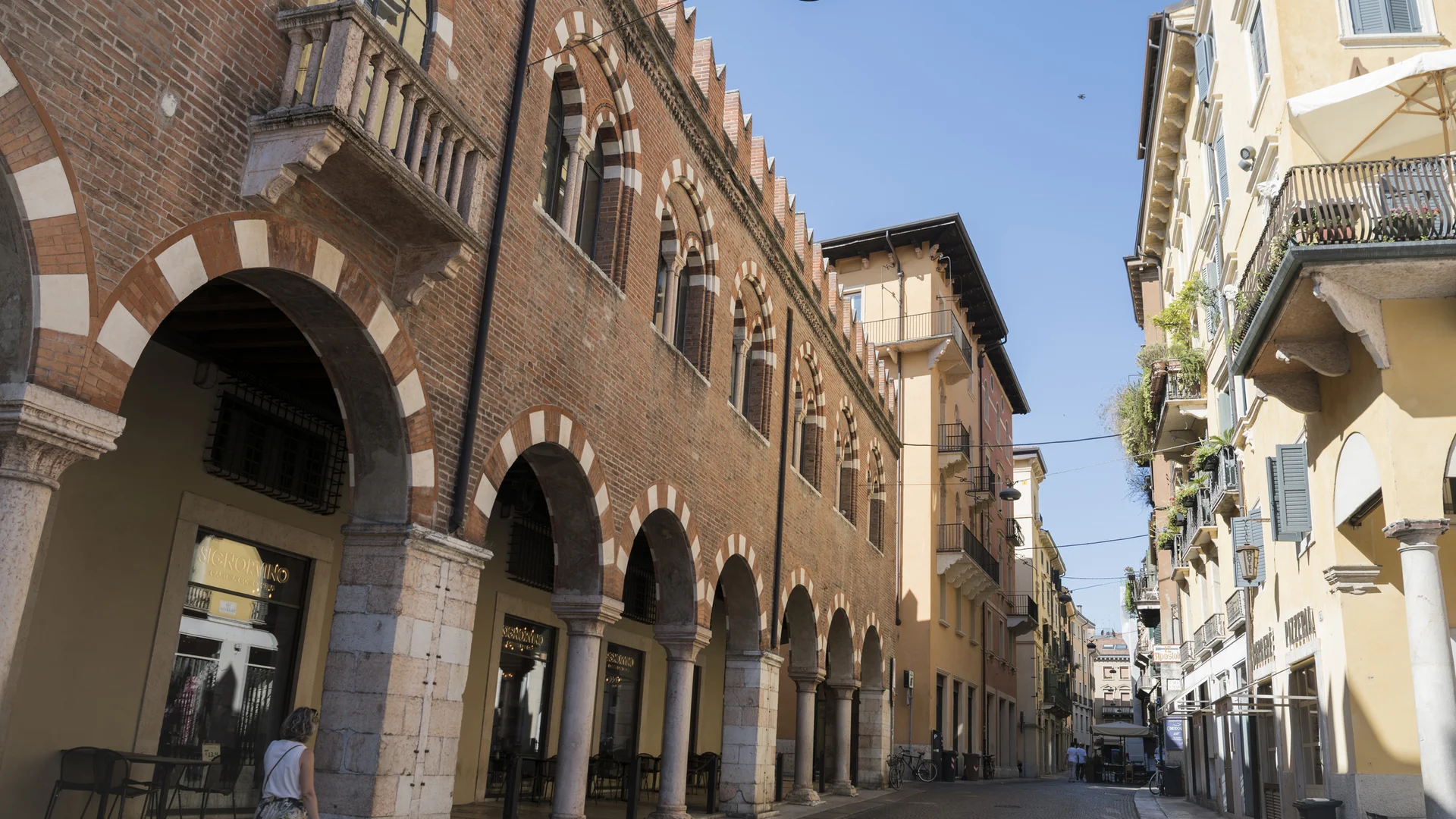 Pedestrian walking along a quiet street lined with historic buildings and arched arcades