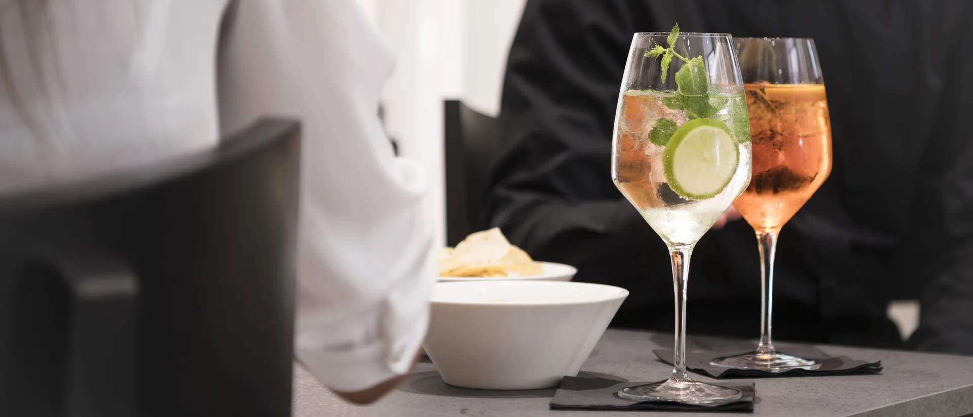 Two drinks with lime and mint sit beside a bowl on a table