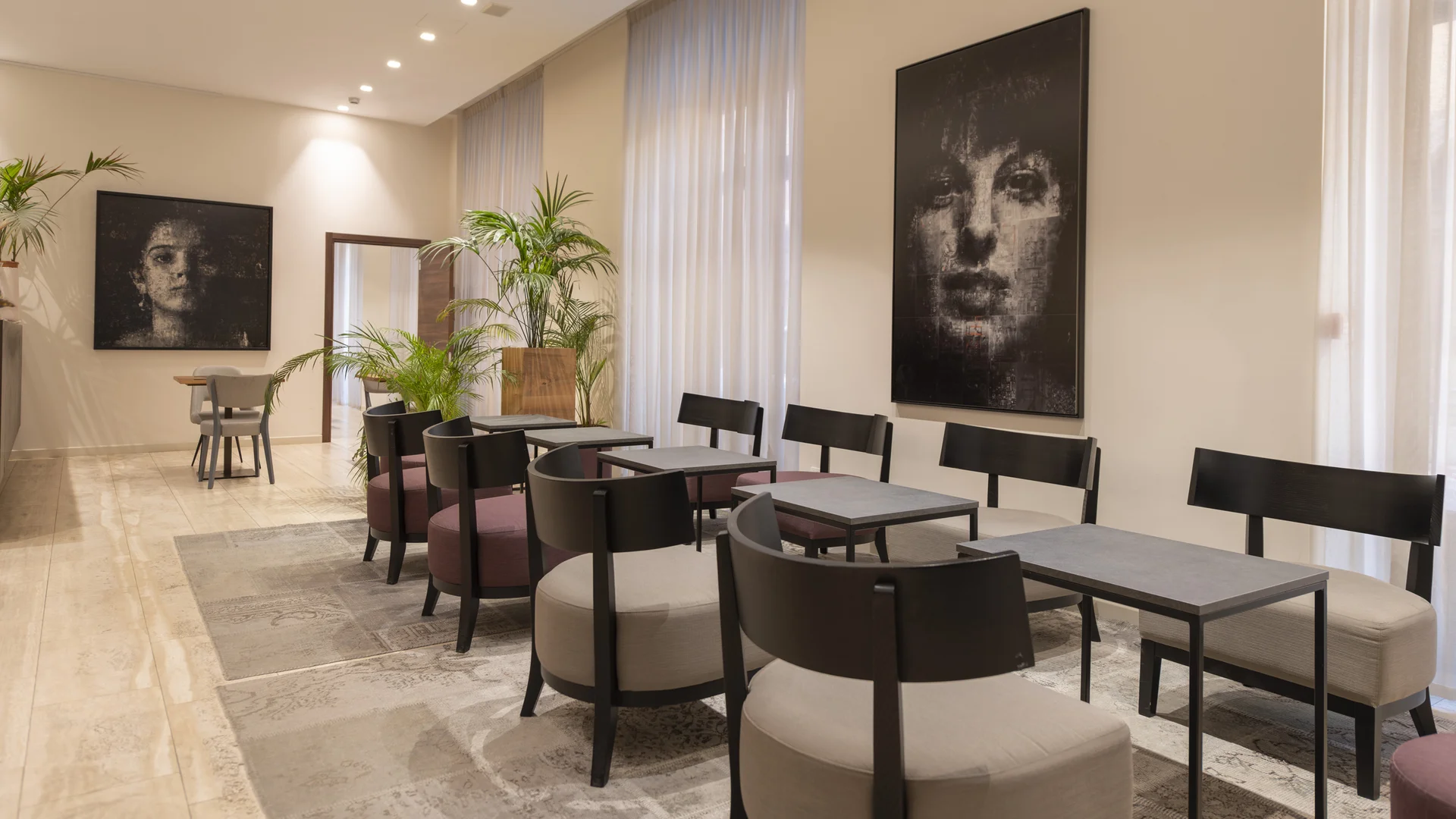Bright hotel lounge with tables, chairs, potted plants and large portrait artworks