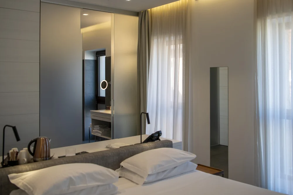 Modern bedroom with a neatly made bed, pillows, mirror and sheer curtains