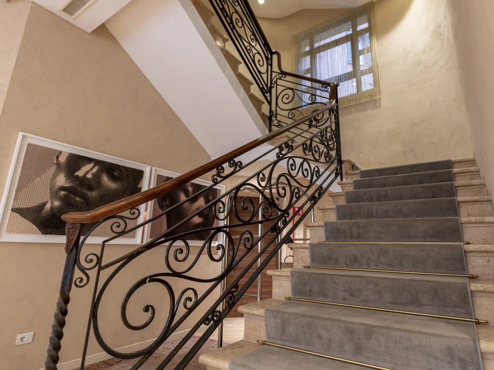 Interior staircase with ornate iron railings, carpeted steps and framed portraits