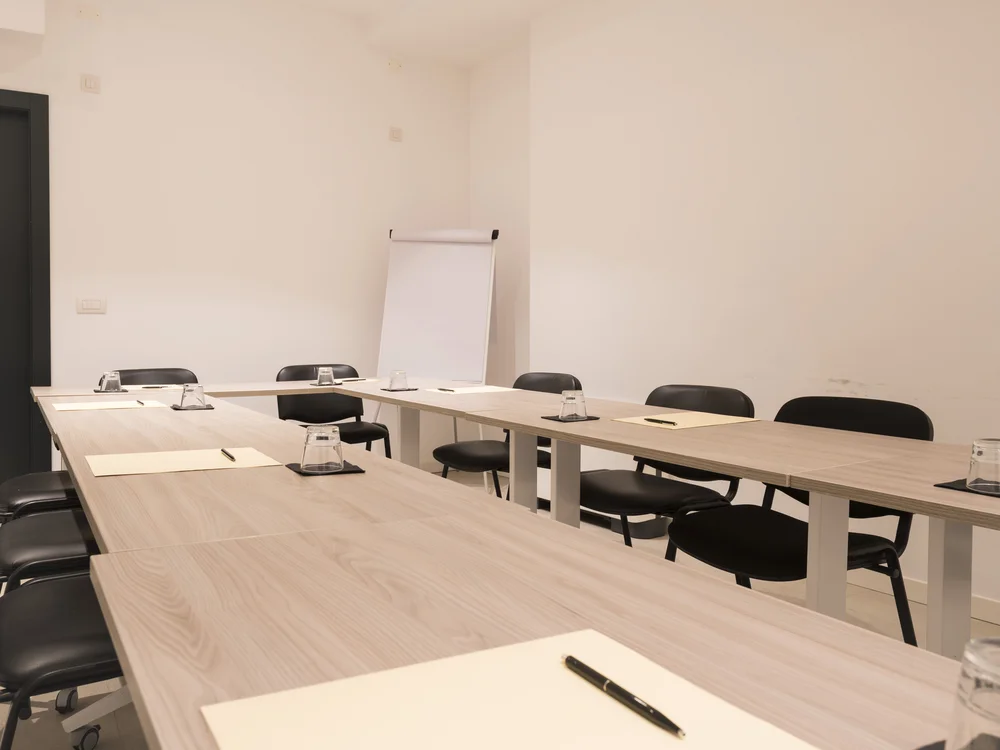 Meeting room with U-shaped tables, chairs, notepads, pens, water glasses and a flip chart