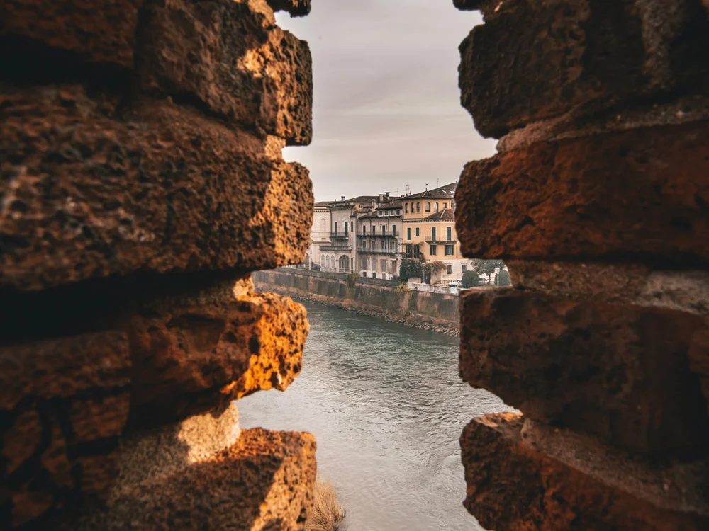 River and colorful riverside buildings viewed through a gap in old brick walls