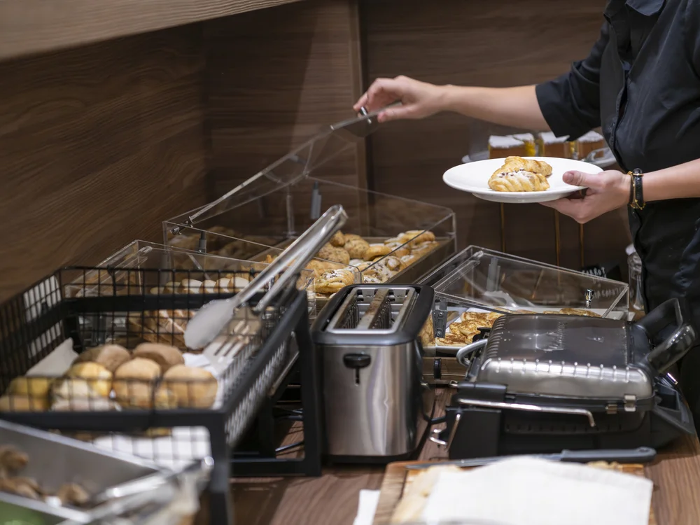 A person serves pastries from a breakfast buffet