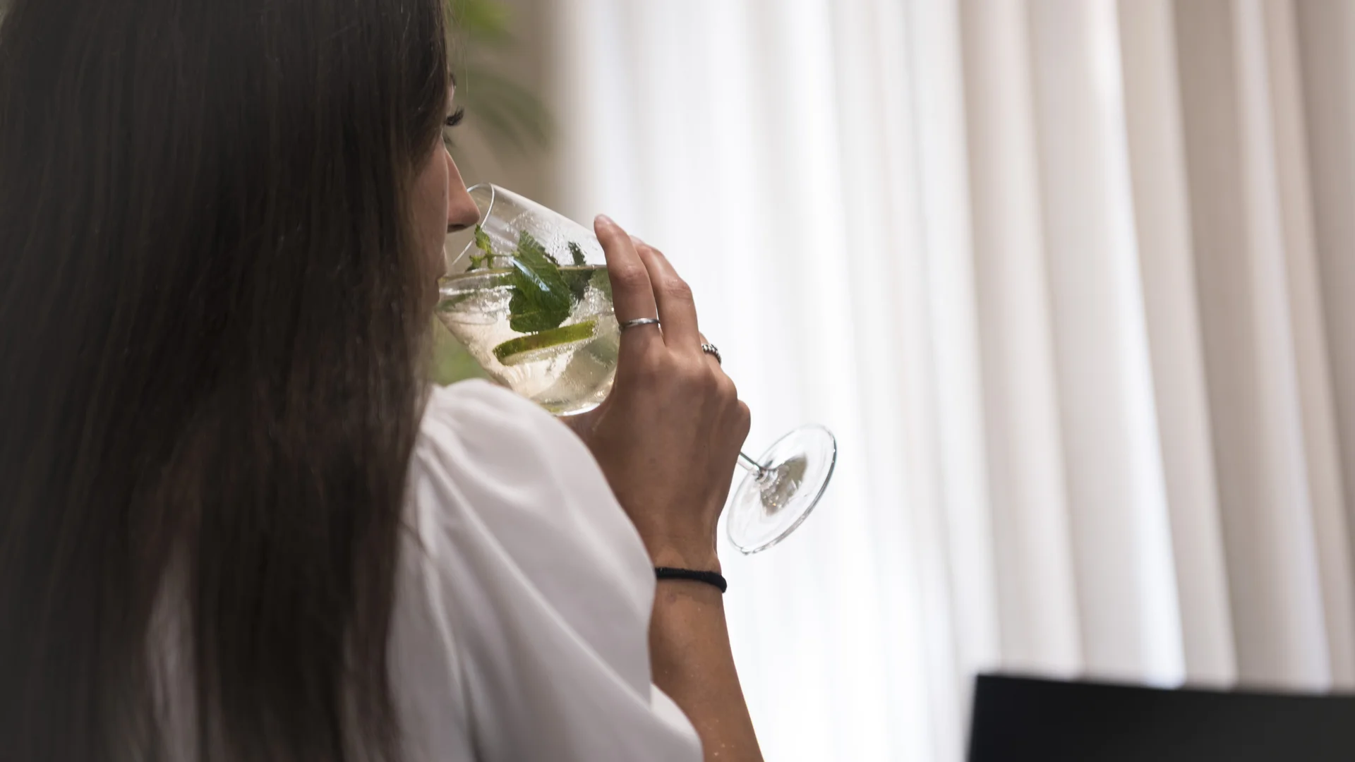 Woman drinking a clear cocktail with green leaves from a stemmed glass