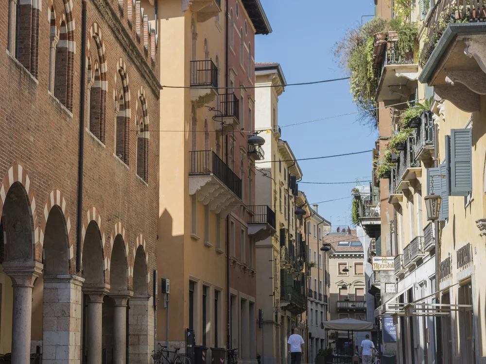 Historic street with brick arcades, balconies, pedestrians and a taxi