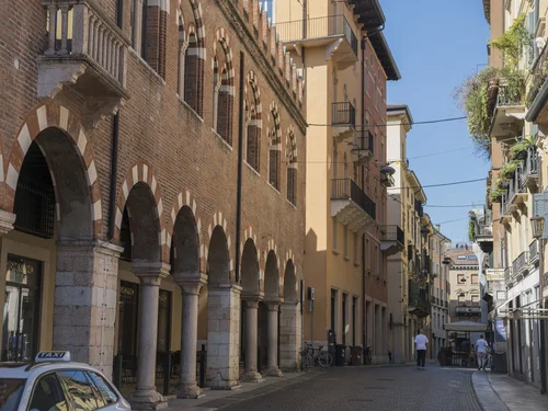 Historic street with brick arcades, balconies, pedestrians and a taxi