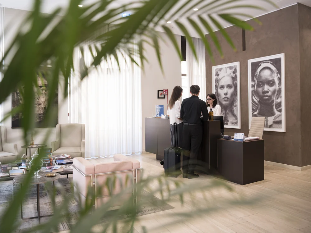 Guests check in at a hotel reception desk beside framed portraits