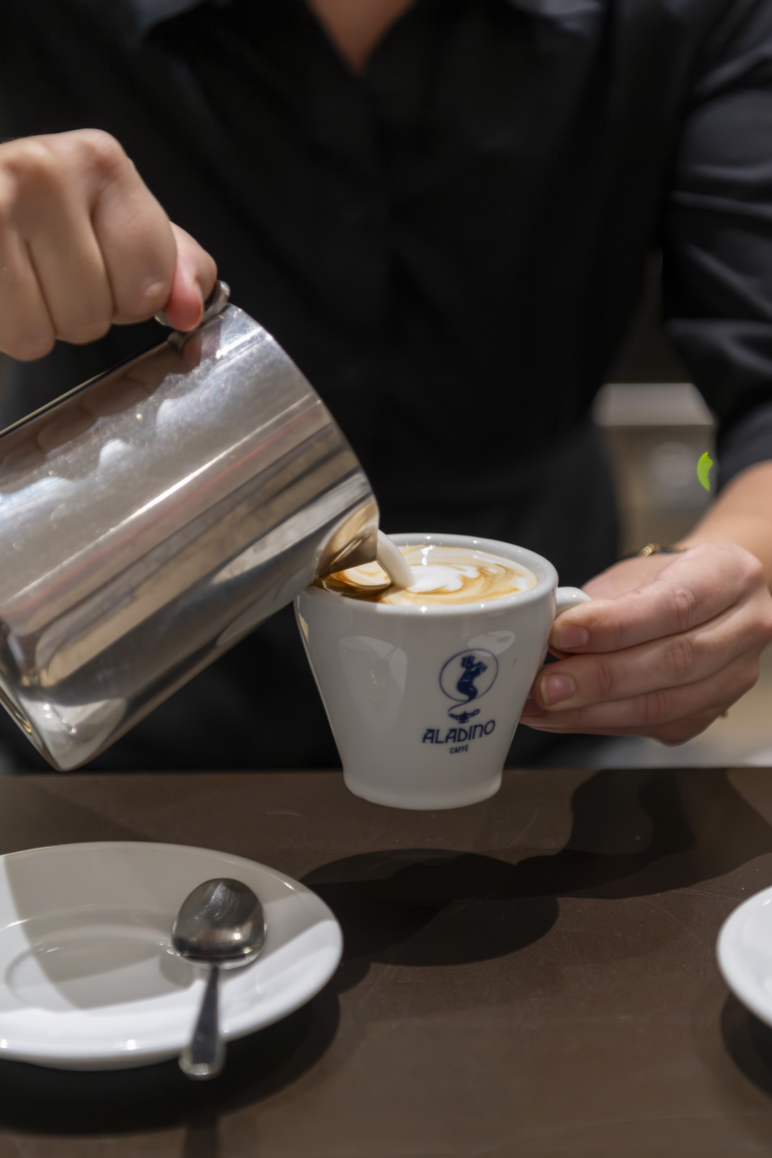 Milk is poured from a metal pitcher into a coffee cup