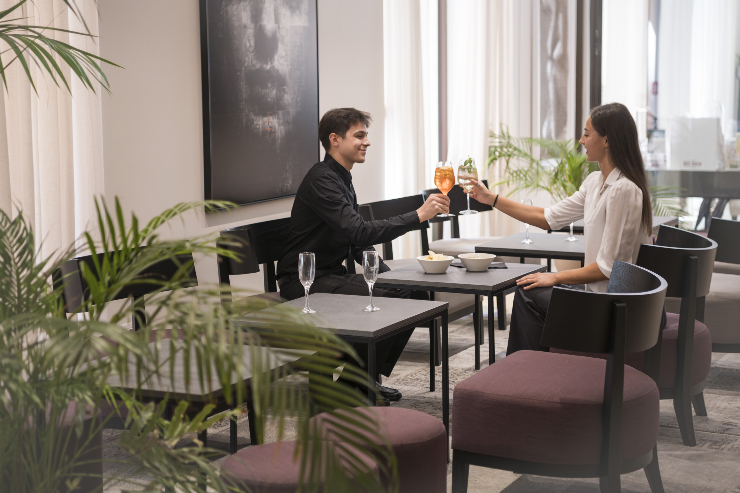 A couple clinks glasses at a table in a bright, modern lounge