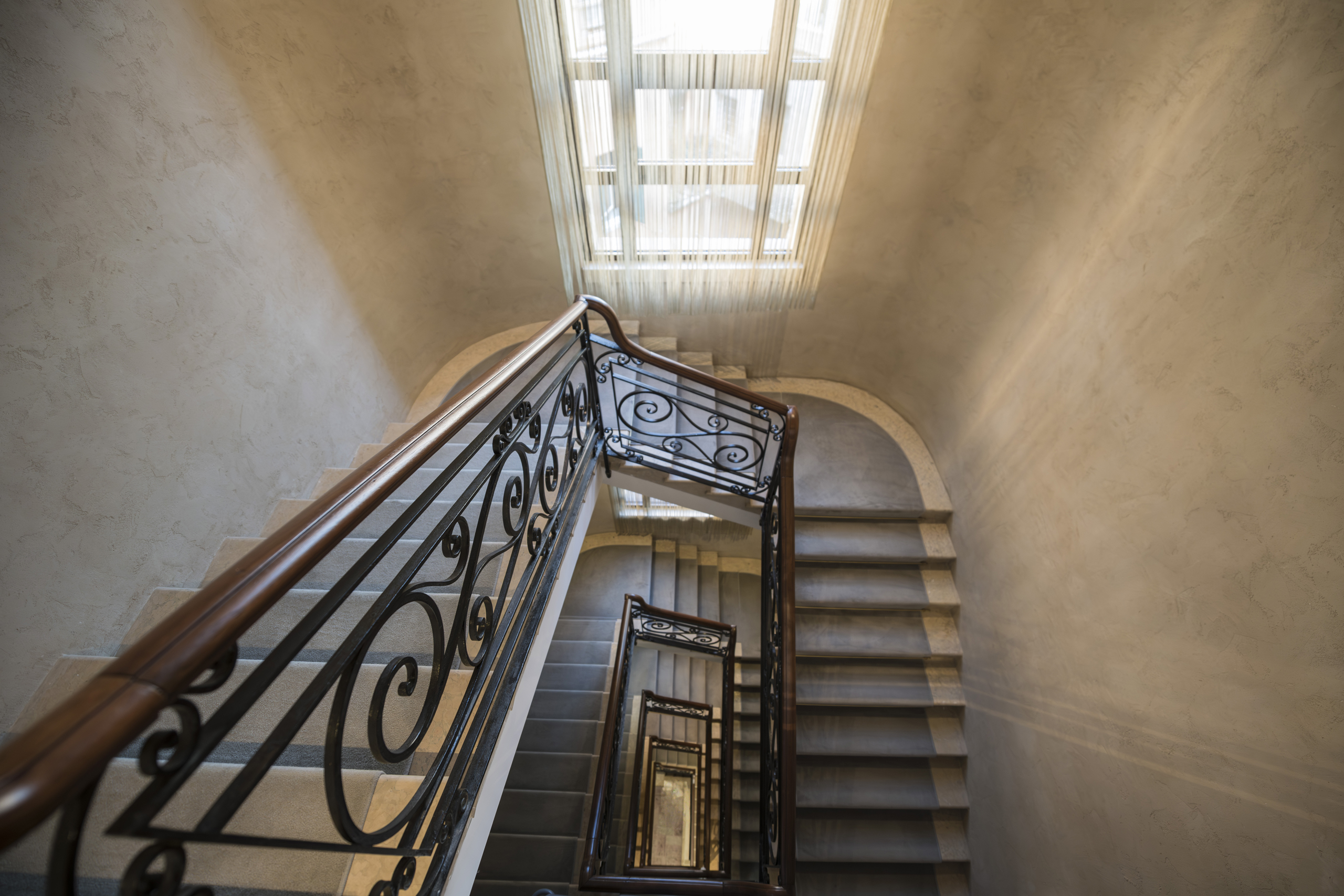 Interior view of a staircase with ornate iron railings beneath a large skylight