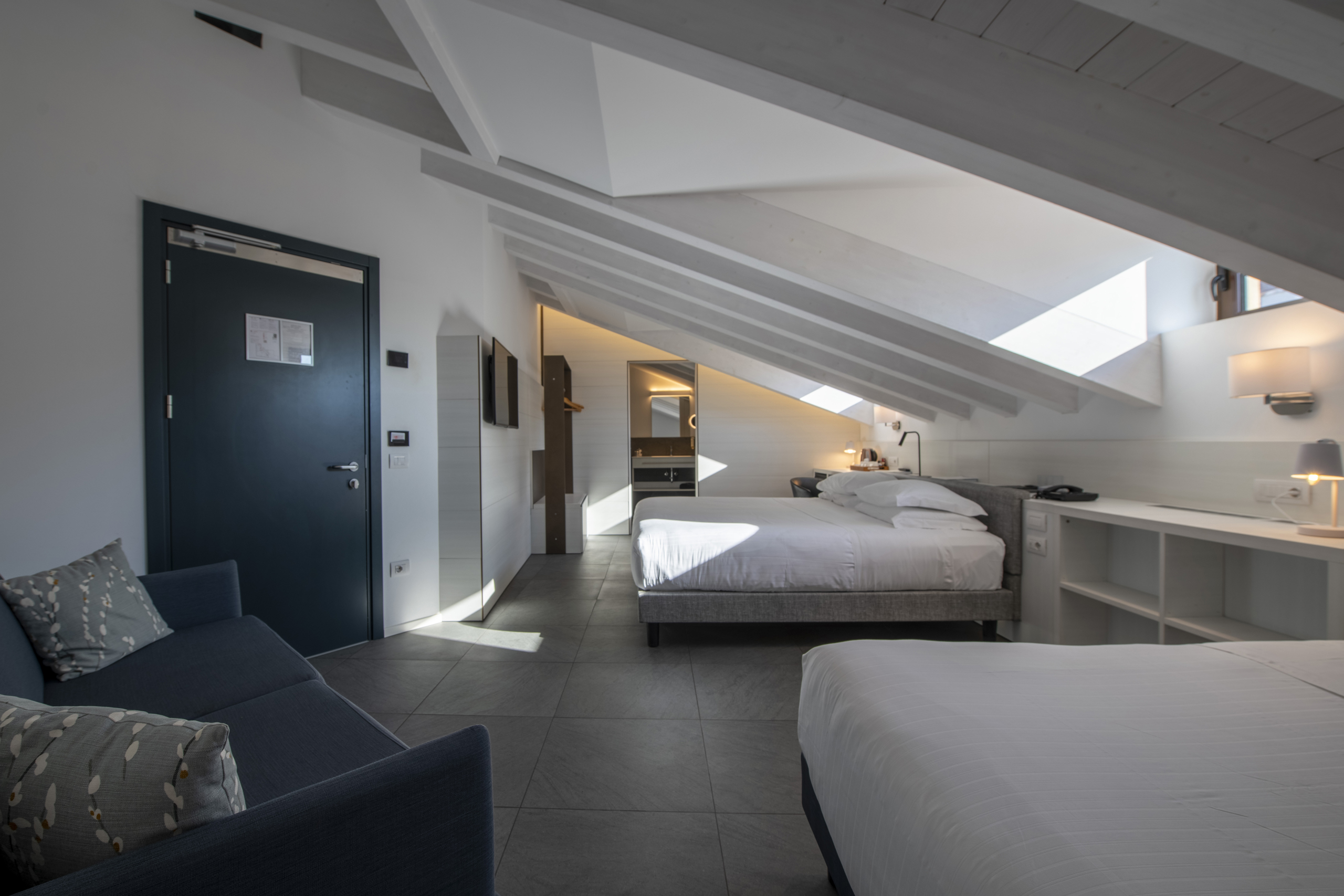 Modern attic hotel room with two beds, a sofa, desk and skylight